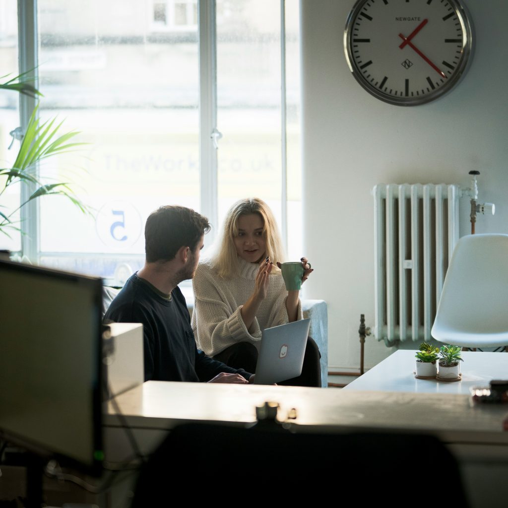 Two colleagues discussing finances over coffee and a laptop in a bright office
