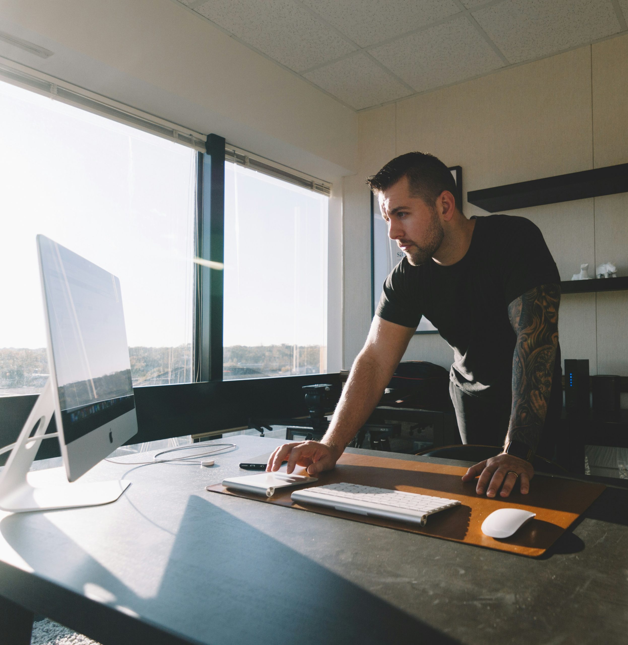 Man working at a standing desk with a desktop computer in a sunny office