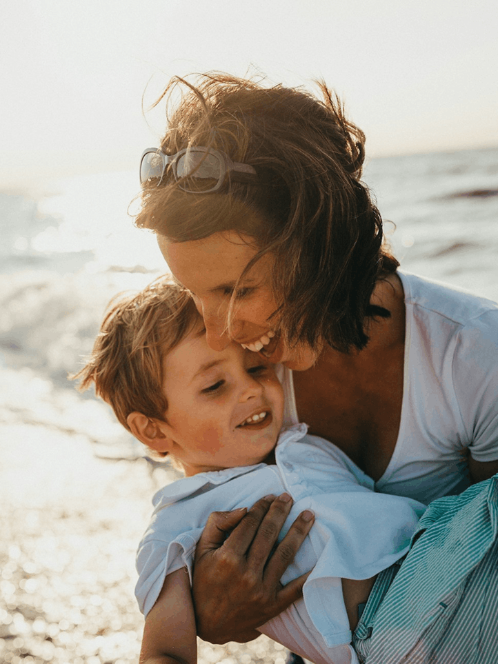 Mother hugging her smiling young son on the beach at sunset