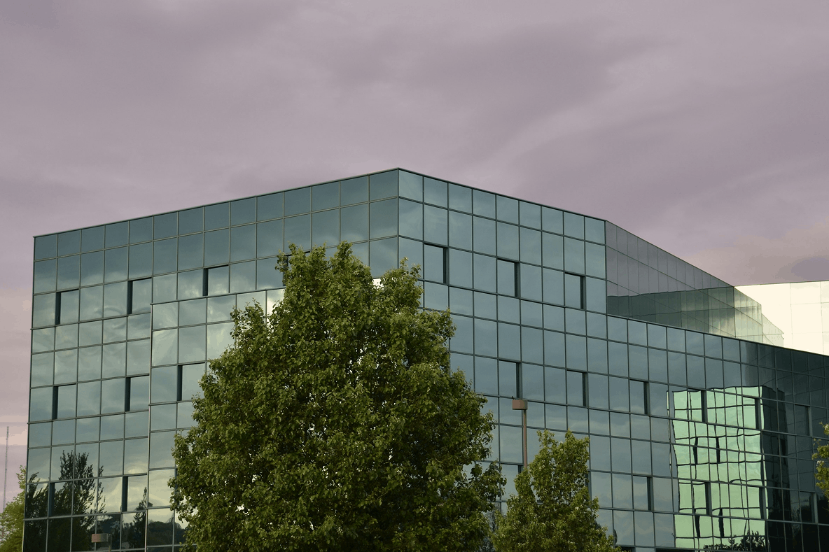 Modern glass office building with green trees under a cloudy purple sky
