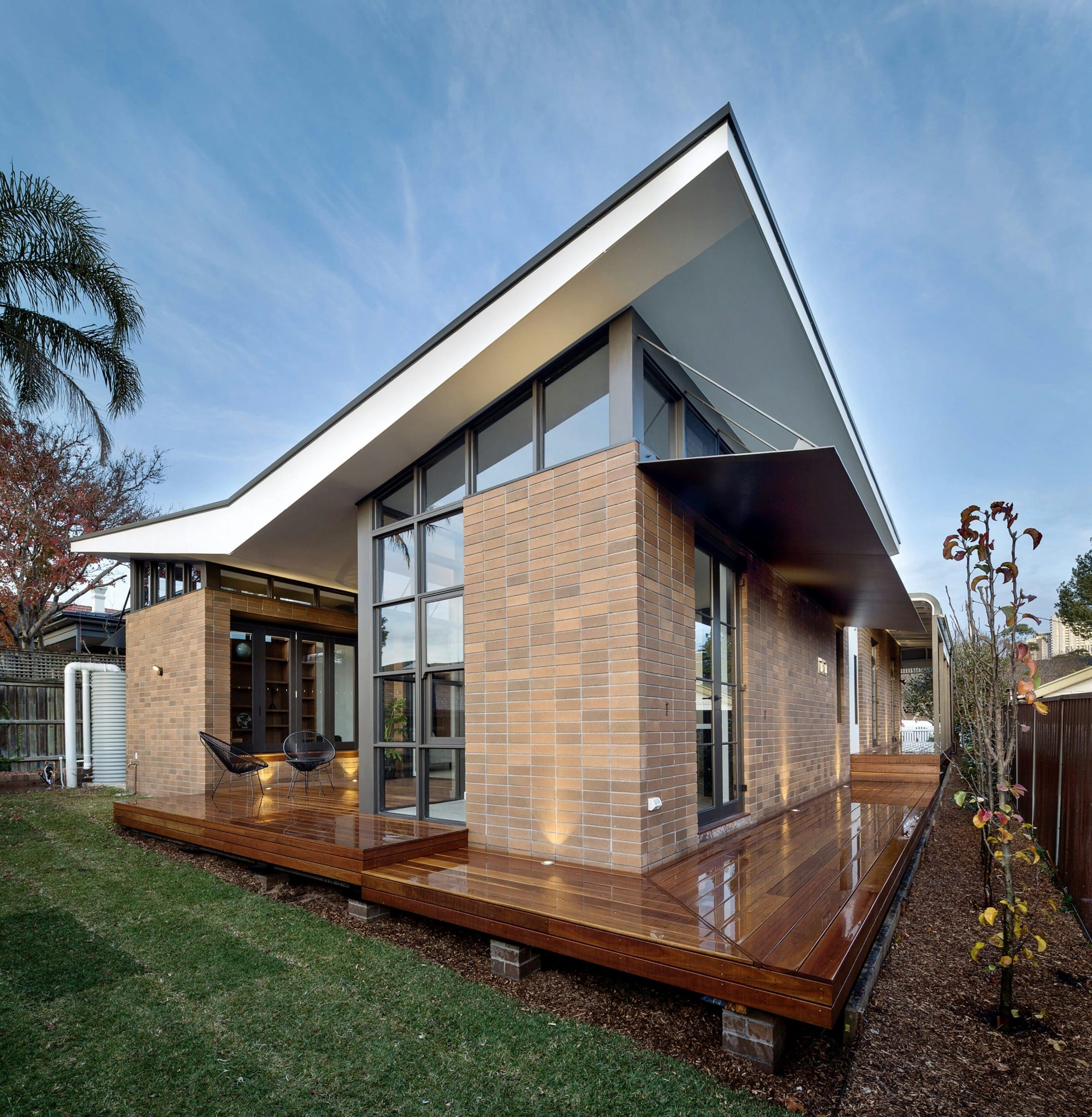 Modern brick house with a steep sloping roof, large glass windows and a timber deck.