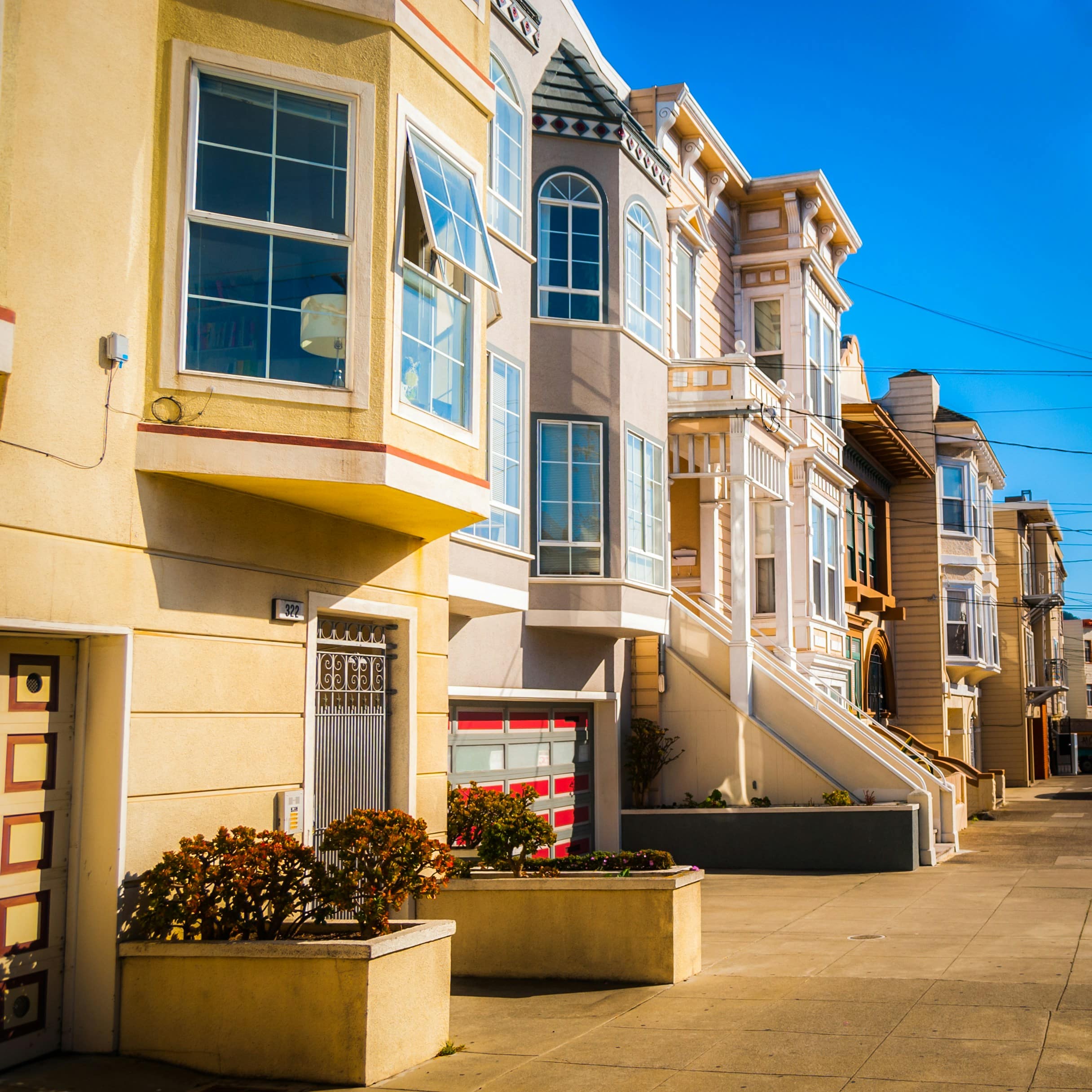 Row of colourful Victorian-style houses along a sunny residential street.