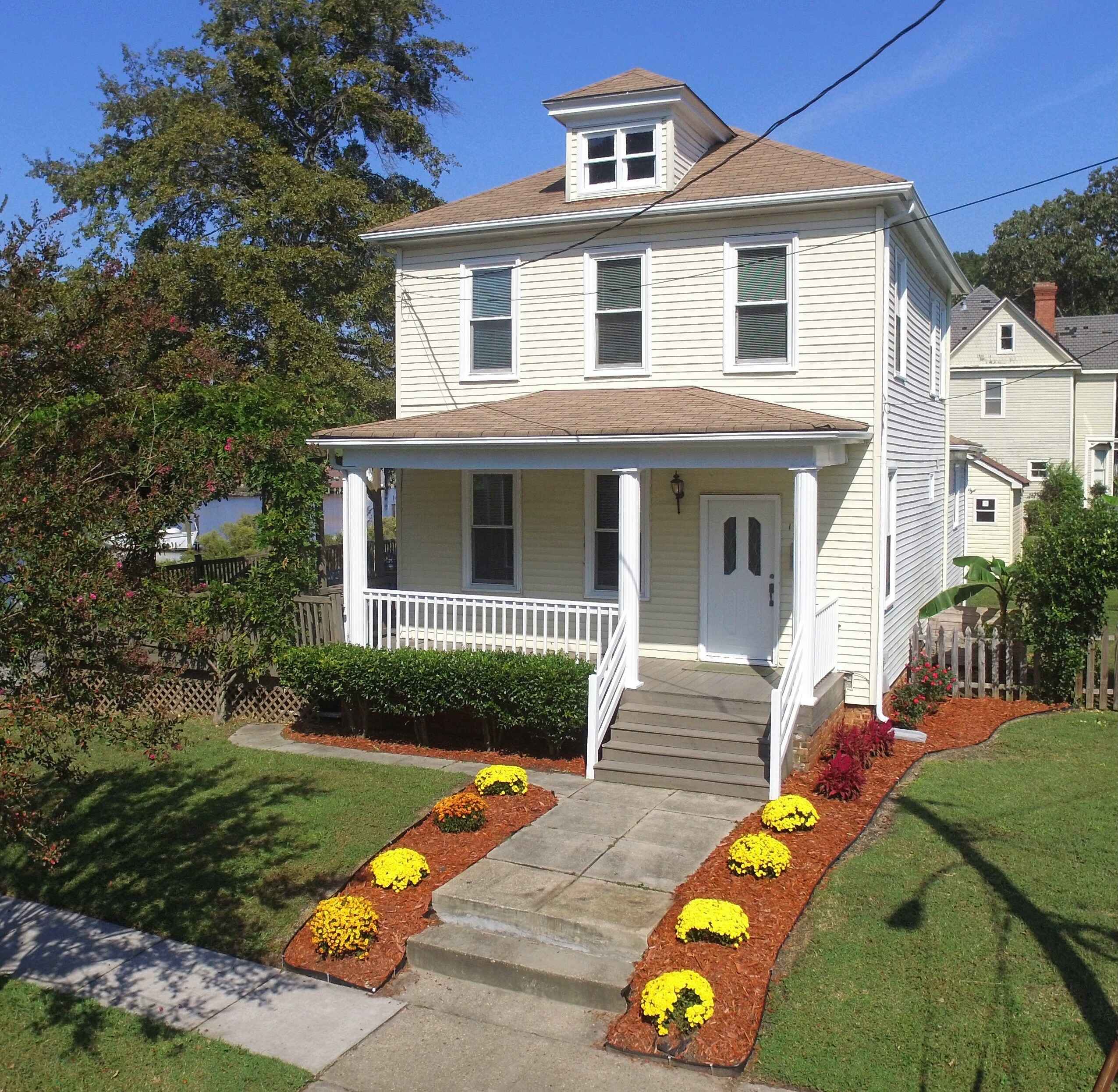Two-storey cream weatherboard home with a front porch and flower garden