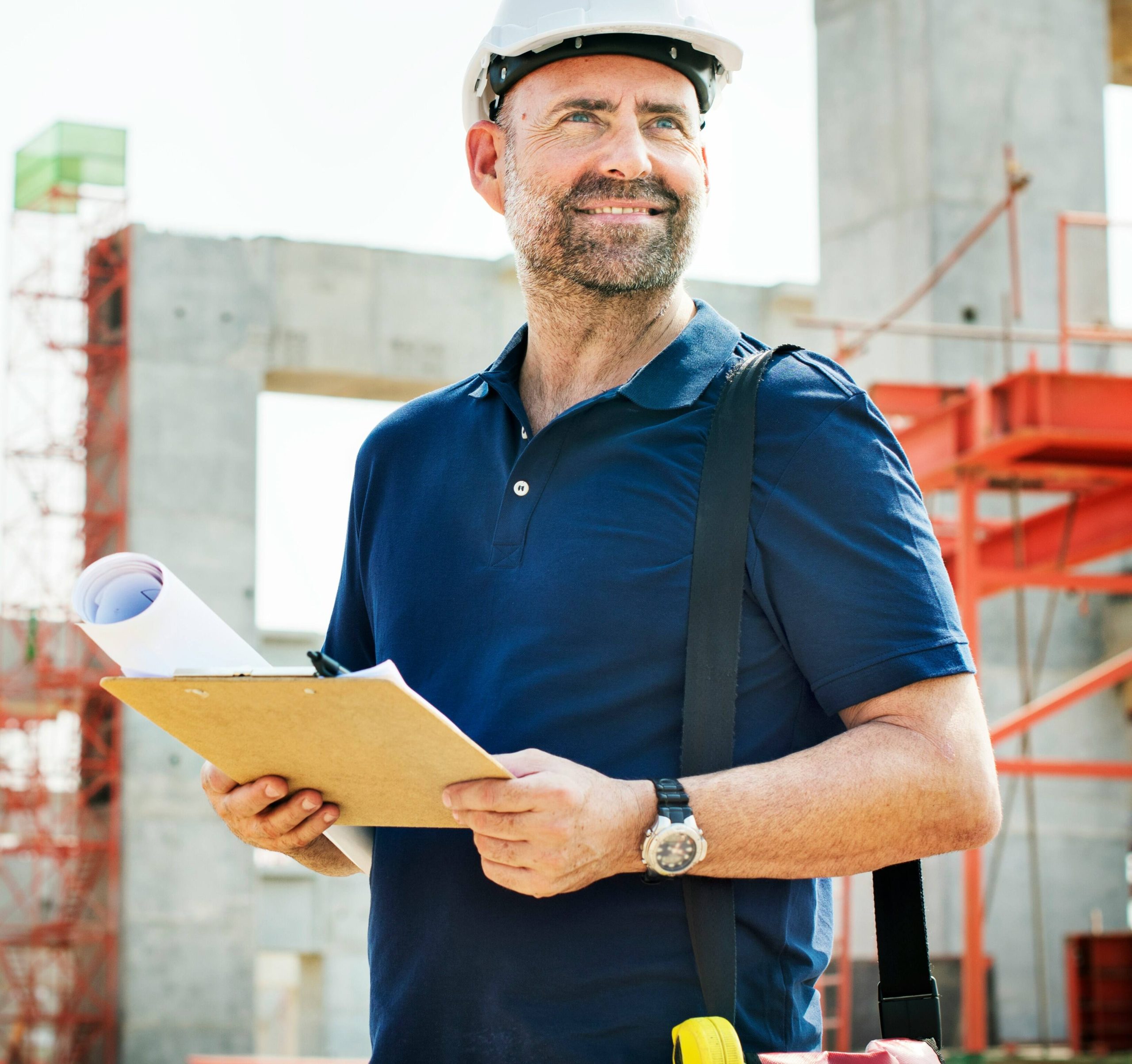 Smiling builder in a hard hat holding plans on a construction site